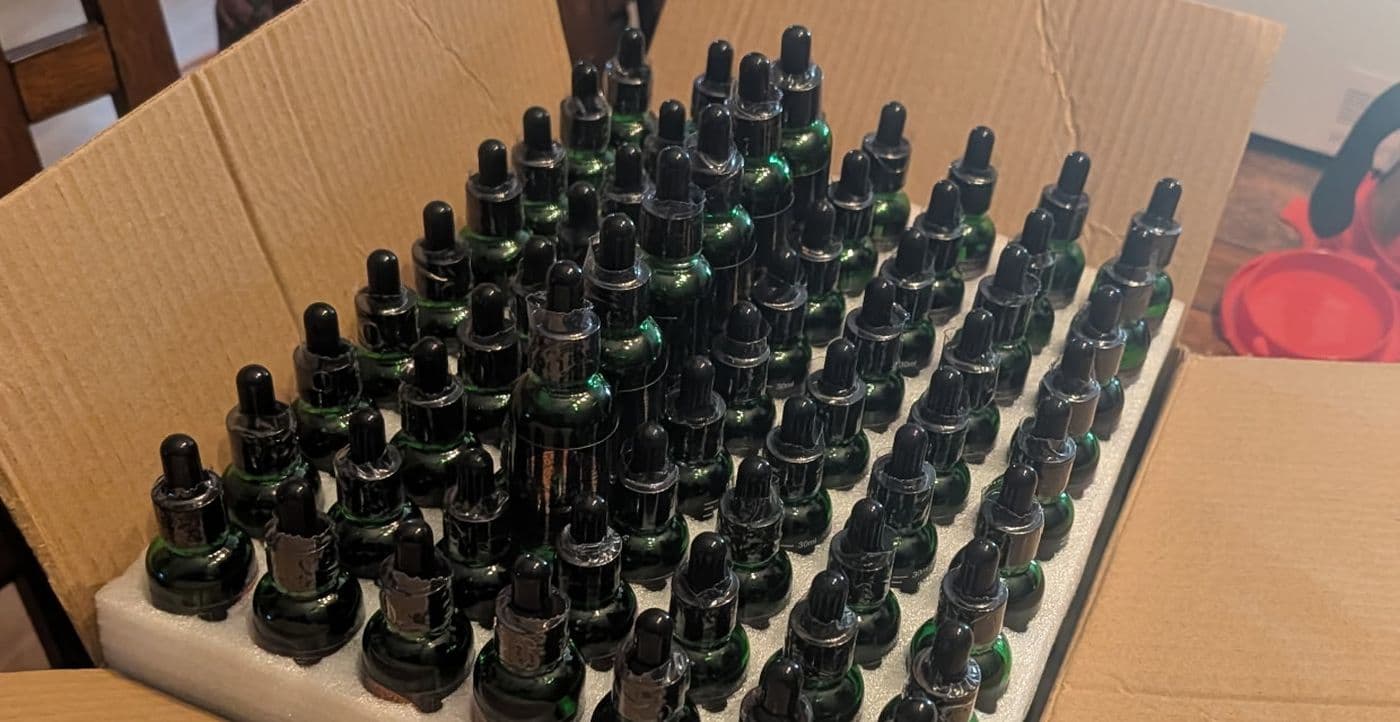 A shipping box packed with rows of freshly filled green dropper bottles